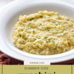 A white bowl of creamy zucchini risotto topped with shredded cheese and herbs sits on a table with an orange napkin underneath.