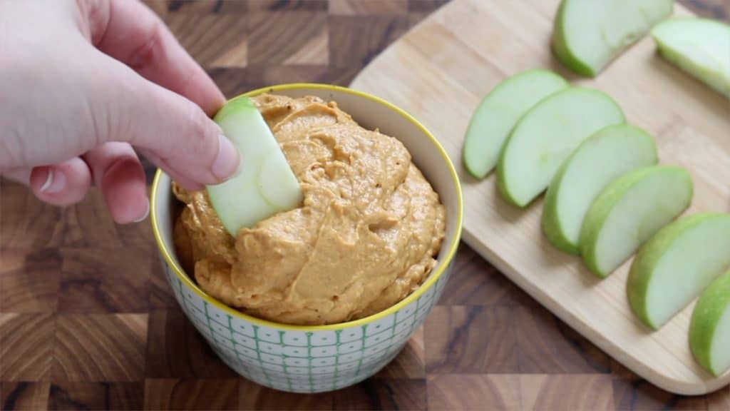 hand dipping an apple slice into pumpkin fruit dip