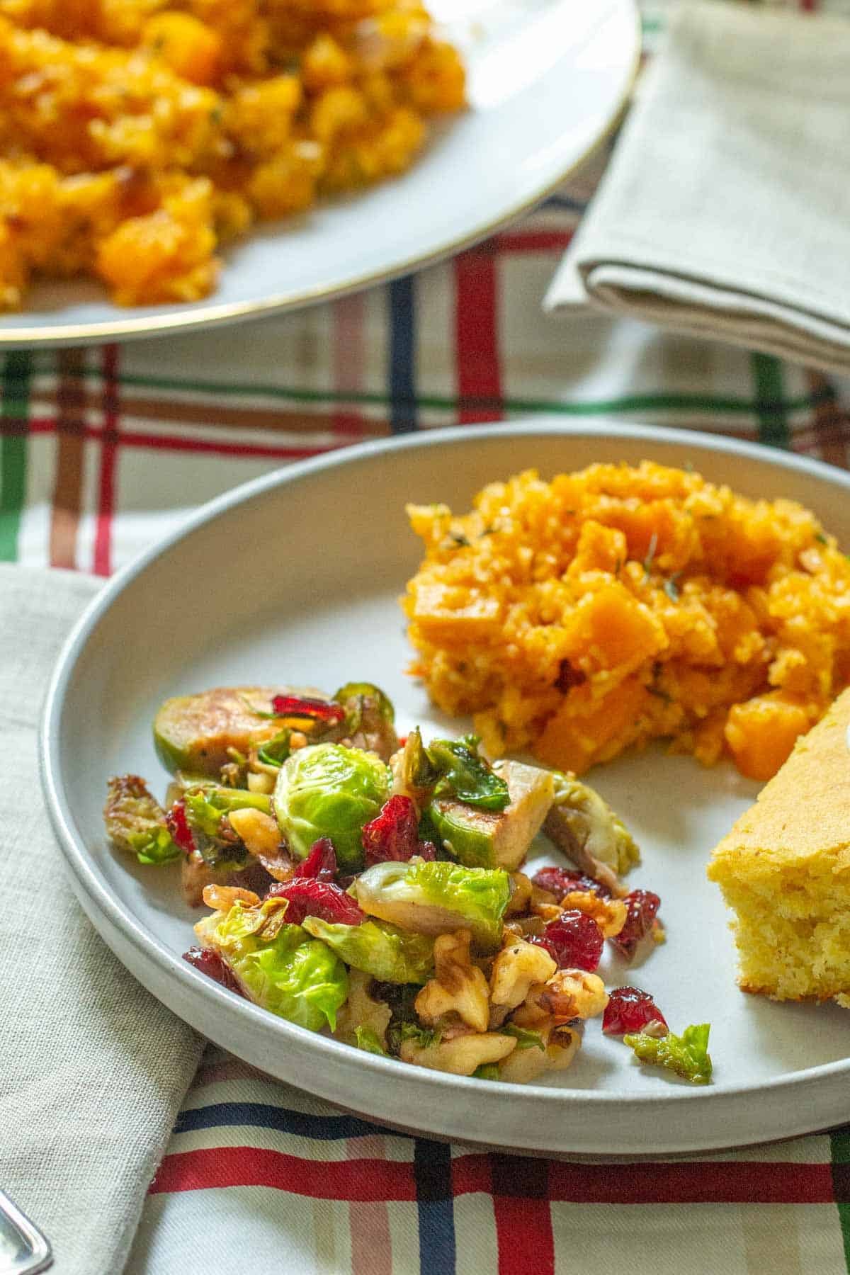 plate with a serving of brussels sprouts with walnuts and cranberries alongside holiday sides
