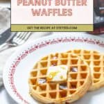 Two peanut butter waffles topped with a pat of butter and syrup sit on a patterned plate, fork and knife nearby. A banner above reads "Peanut Butter Waffles," highlighting this delicious breakfast treat.