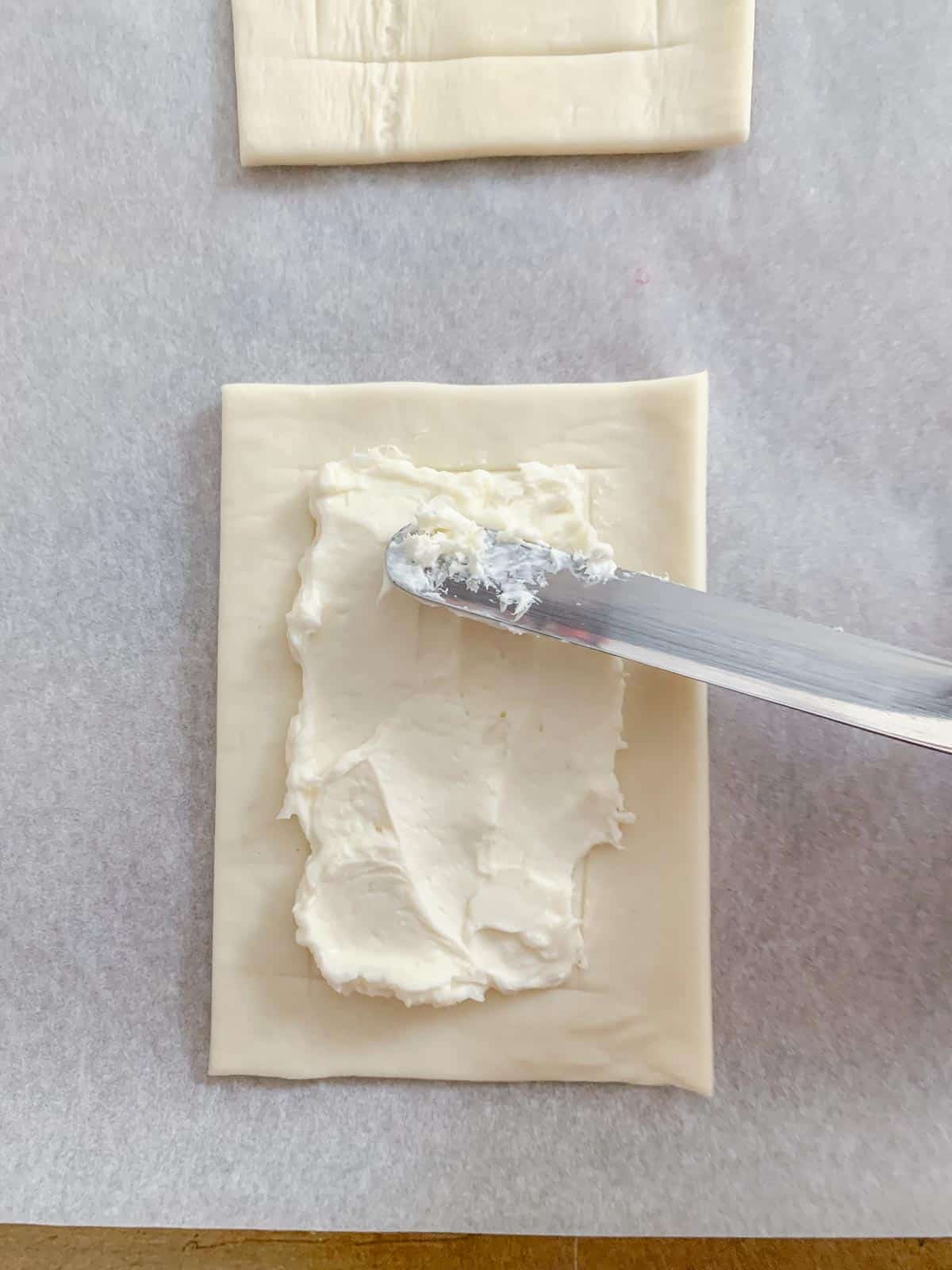 cream cheese being spread onto puff pastry
