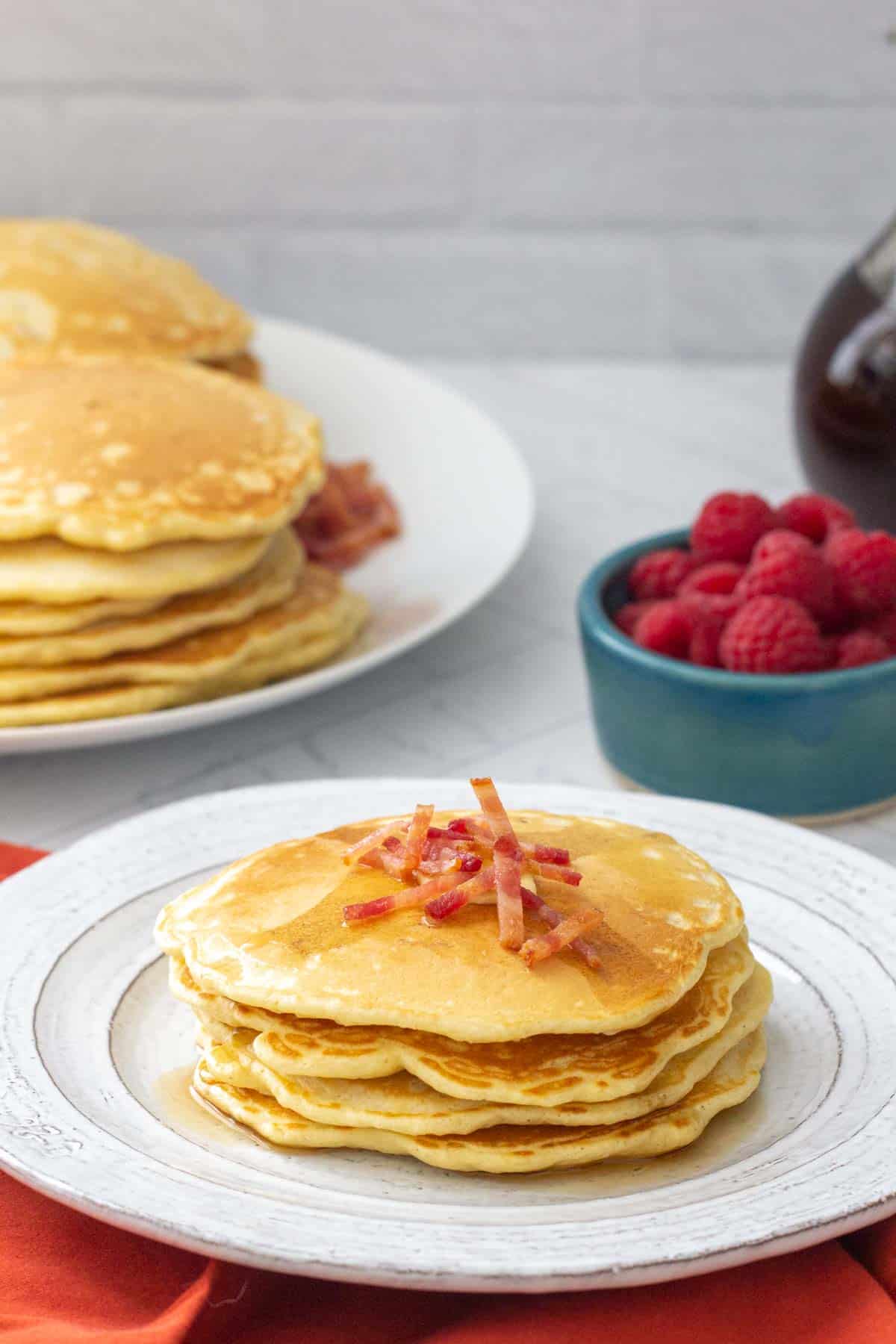 plate of bacon pancakes with stacked pancakes behind