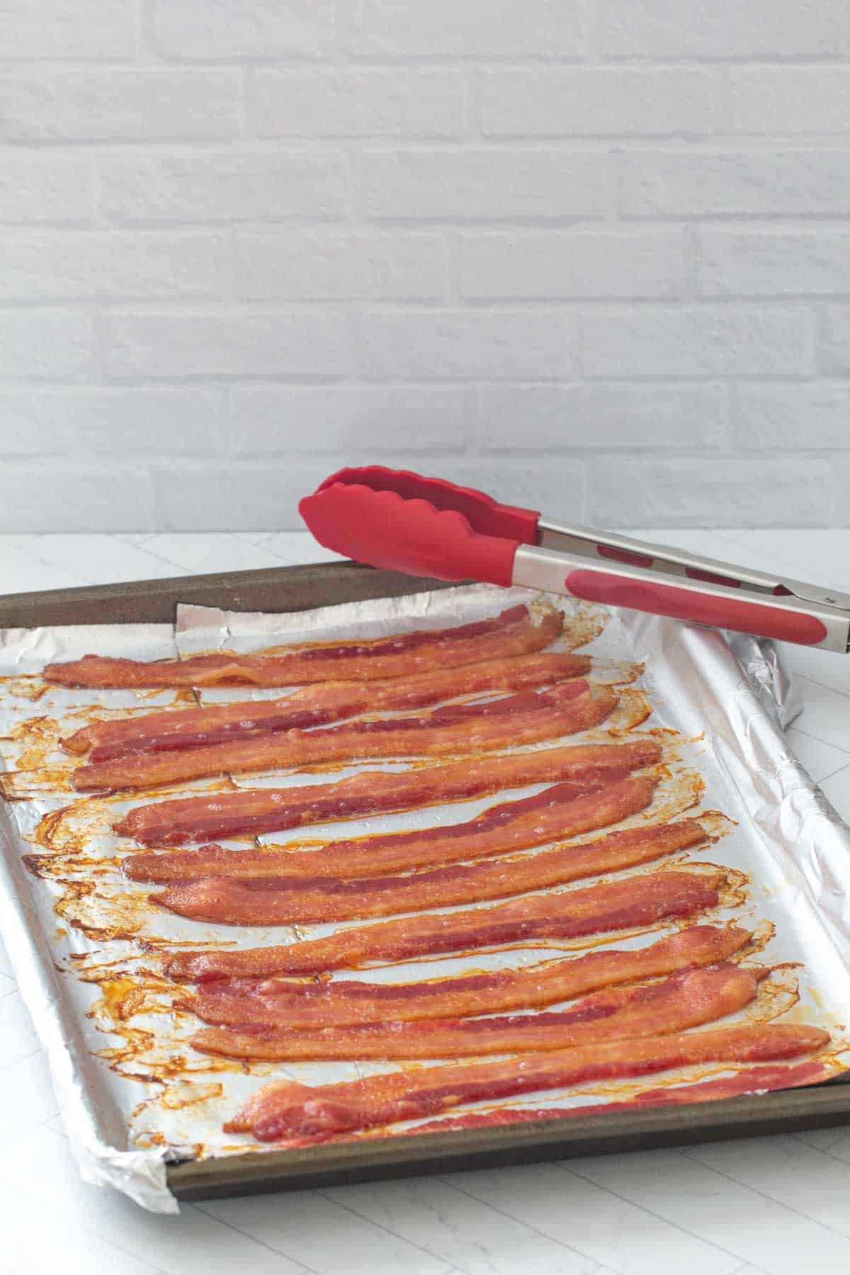 cooked bacon on baking sheet with tongs