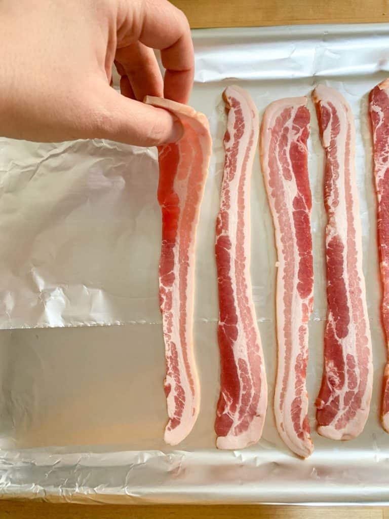 placing uncooked bacon on baking sheet
