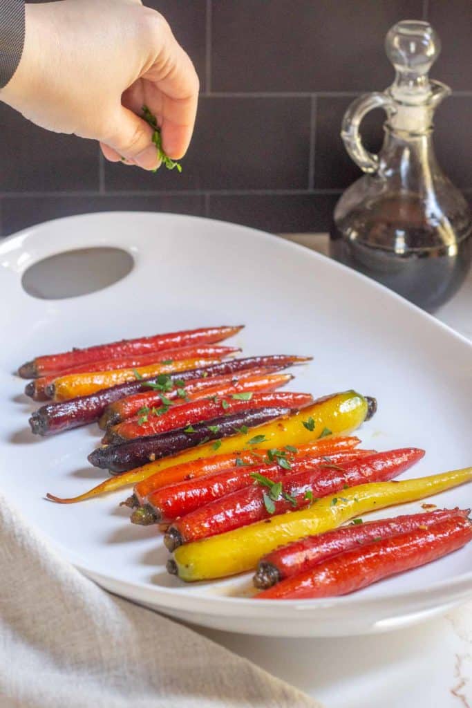 glazed carrots on a serving plate with hand sprinkling parsley