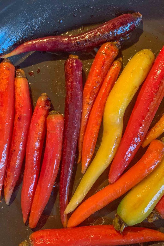 Assorted colorful carrots being sautéed in a pan with oil for delicious maple glazed carrots.