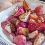 hand holding a bowl of roasted radishes