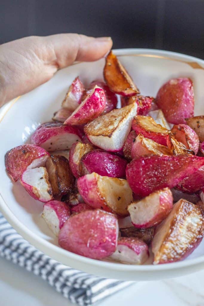 hand holding a bowl of roasted radishes