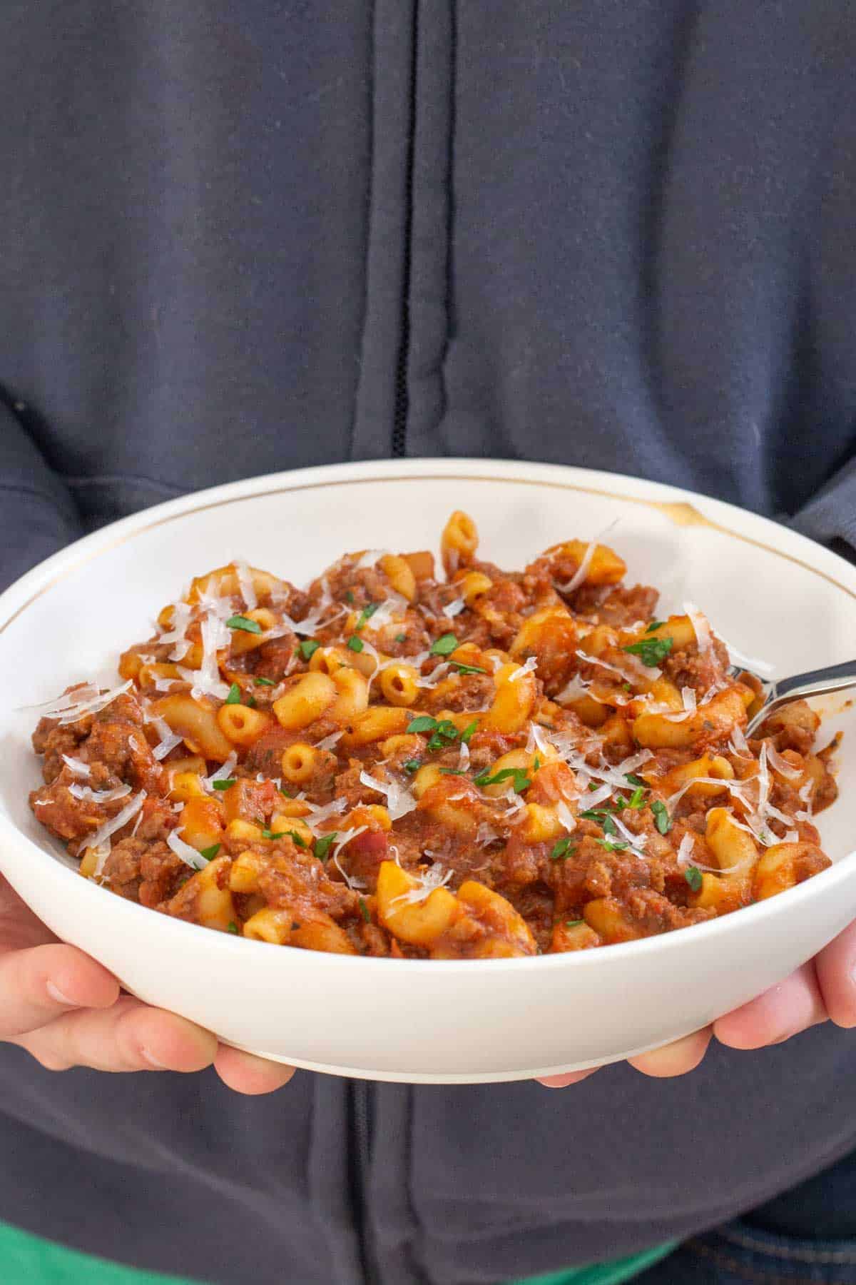 hands holding bowl of American goulash