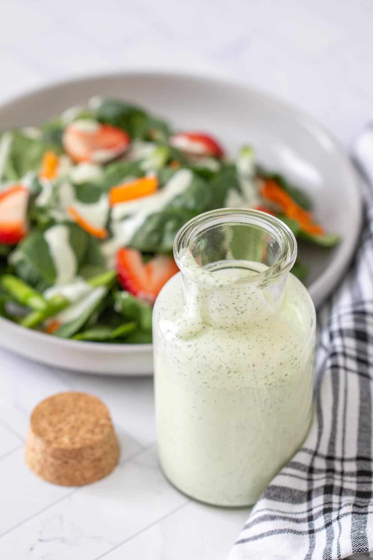 bottle of green goddess dressing with salad behind