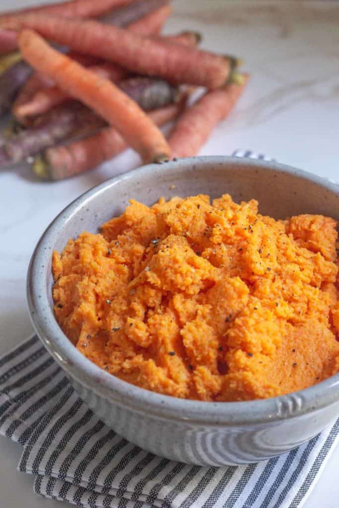 mashed carrots in bowl with carrots behind