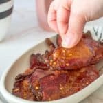 fingers picking up candied bacon slice