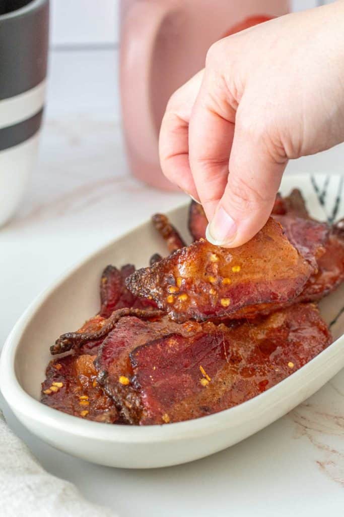 fingers picking up candied bacon slice