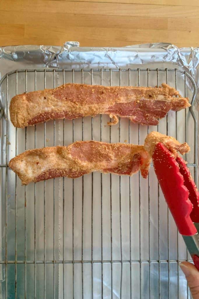 tongs laying millionaire bacon onto baking sheet