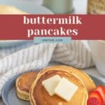 A plate of fluffy buttermilk pancakes topped with two pats of butter, served with fresh strawberry slices on the side.