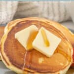 Stack of fluffy buttermilk pancakes topped with two pats of butter and drizzled with syrup on a gray plate.