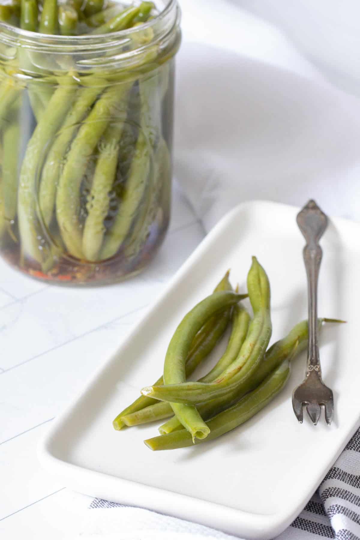 pickled green beans on plate with jar beside