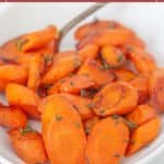 A white bowl filled with honey roasted carrots, sliced and garnished with fresh herbs, sits invitingly with a spoon in the background.