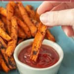A hand dips a roasted carrot fry into a small dish of ketchup, with more crispy carrot fries piled on a blue plate in the background.