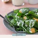 A plate of spinach salad with croutons is drizzled with creamy garlic dressing, alongside a jar of the same in the background. Text reads: "easy creamy garlic dressing.