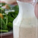 A glass pitcher filled with creamy garlic dressing sits in front of a plate of salad greens. Text overlay reads "Creamy Garlic Dressing" and "stetted.com," showcasing the perfect topping for your next salad.