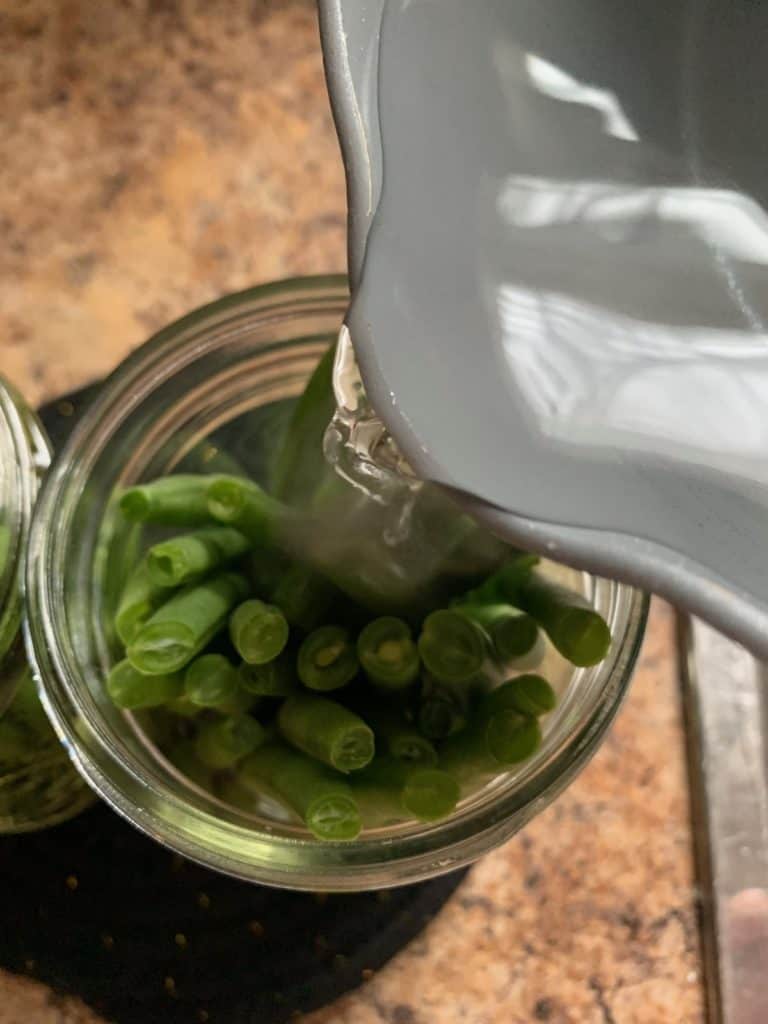 pouring brine into jar of green beans