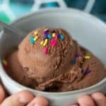 child hands holding bowl of chocolate ice cream with sprinkles