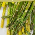 Close-up of parmesan asparagus spears, perfectly cooked and topped with grated cheese, with text overlay reading "parmesan asparagus" and "quick & easy side dish.