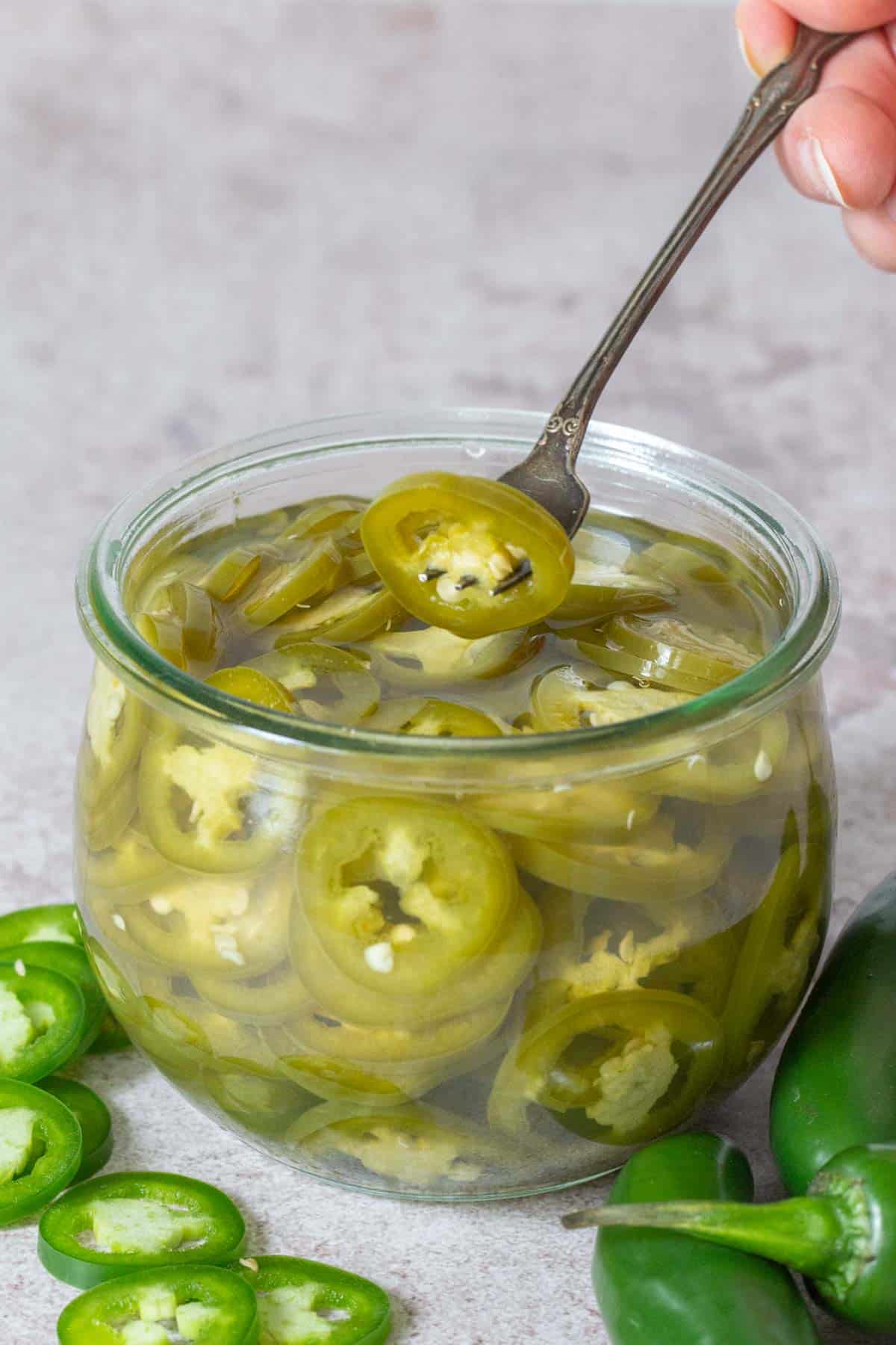 fork holding pickled jalapeño over jar