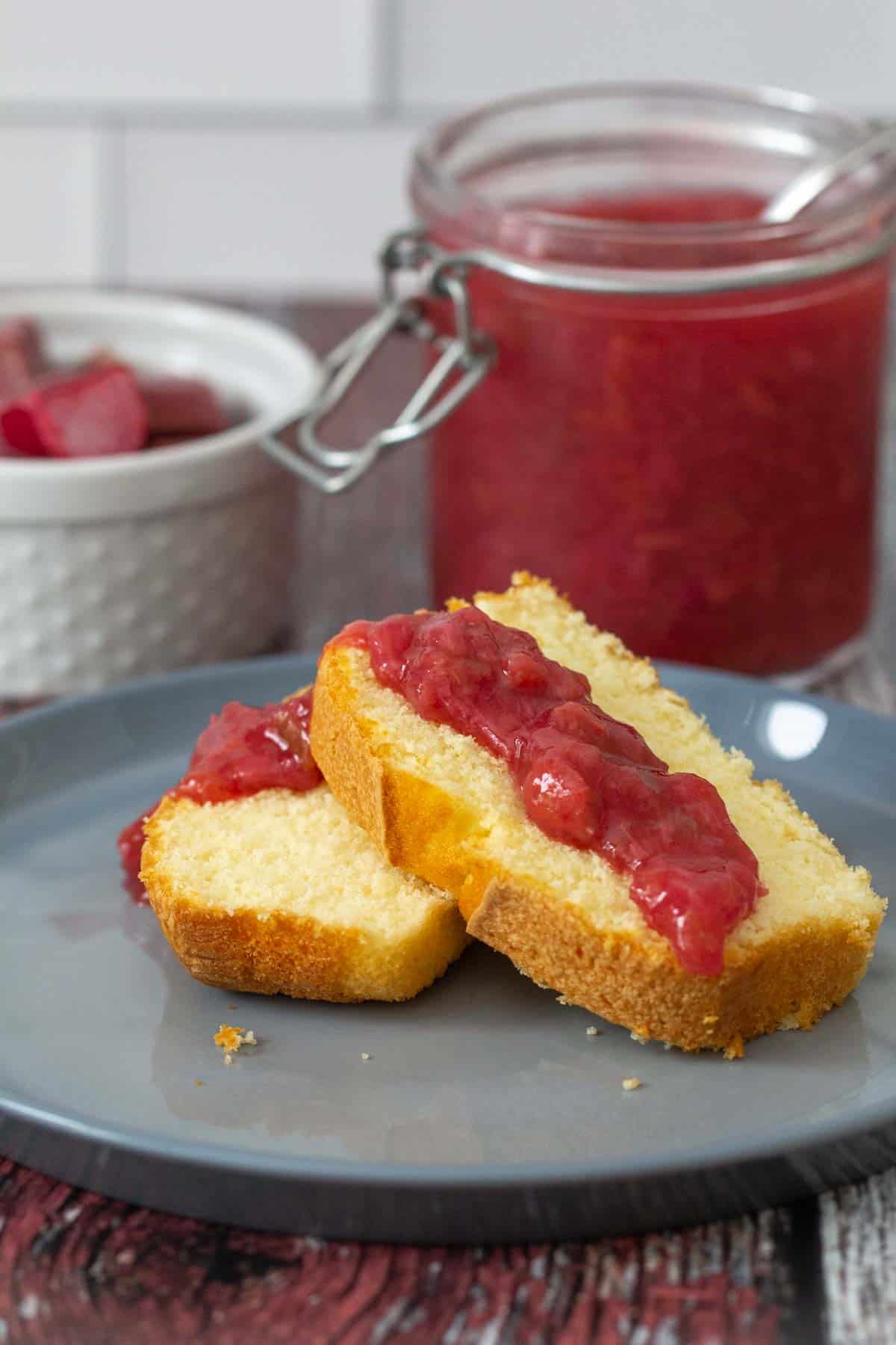 rhubarb sauce spooned onto pound cake with jar and rhubarb behind