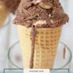 A scoop of rocky road ice cream, packed with chunks of nuts and marshmallow, sits in a crisp waffle cone held upright in a glass.