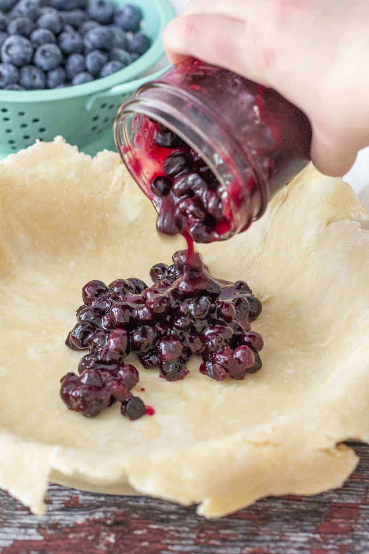 pouring blueberry pie filling into crust