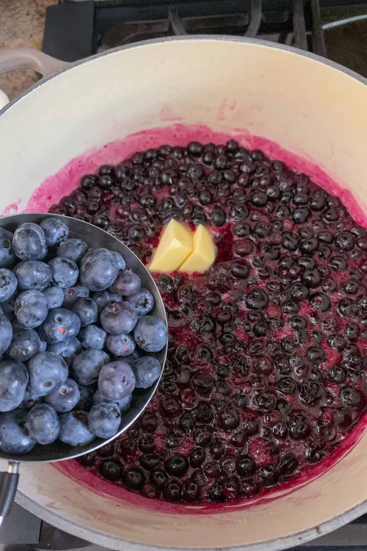 adding blueberries and butter to blueberry pie filling
