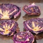 Four slices of roasted purple cabbage on a baking sheet, slightly caramelized, create the perfect cabbage steaks, with a “roasted cabbage steaks” label at the bottom.