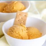 Two scoops of pumpkin ice cream and a rectangular graham cracker are served in a white bowl, highlighting the creamy texture of the pumpkin ice cream. Another bowl with more pumpkin ice cream sits in the background.