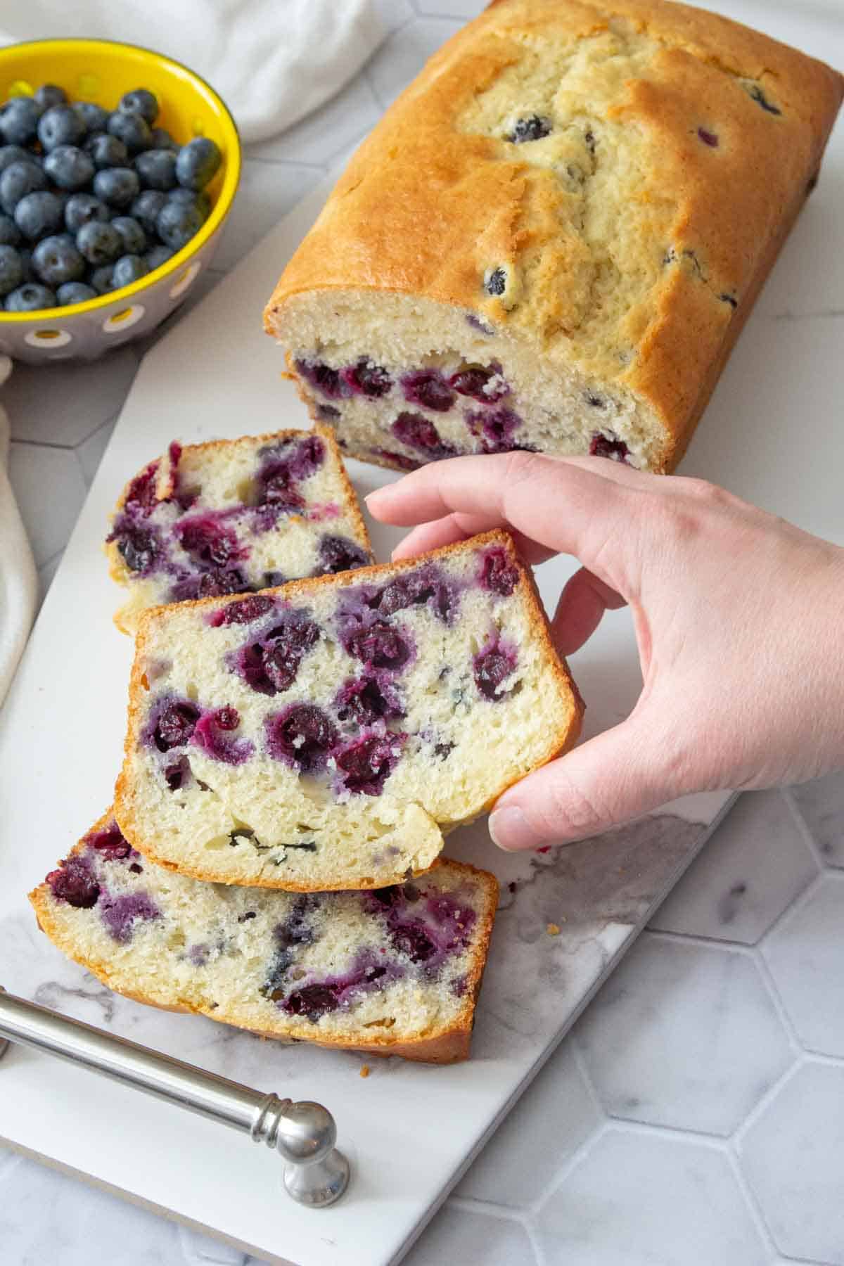 hand picking up slice of blueberry bread