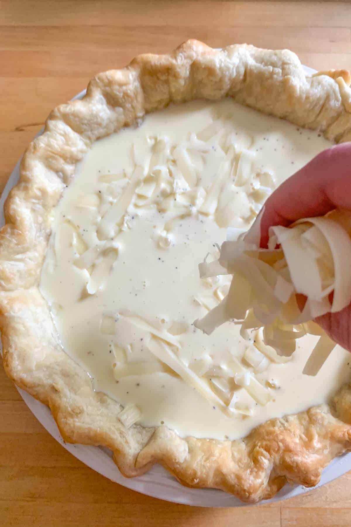 adding cheese to unbaked cheese quiche