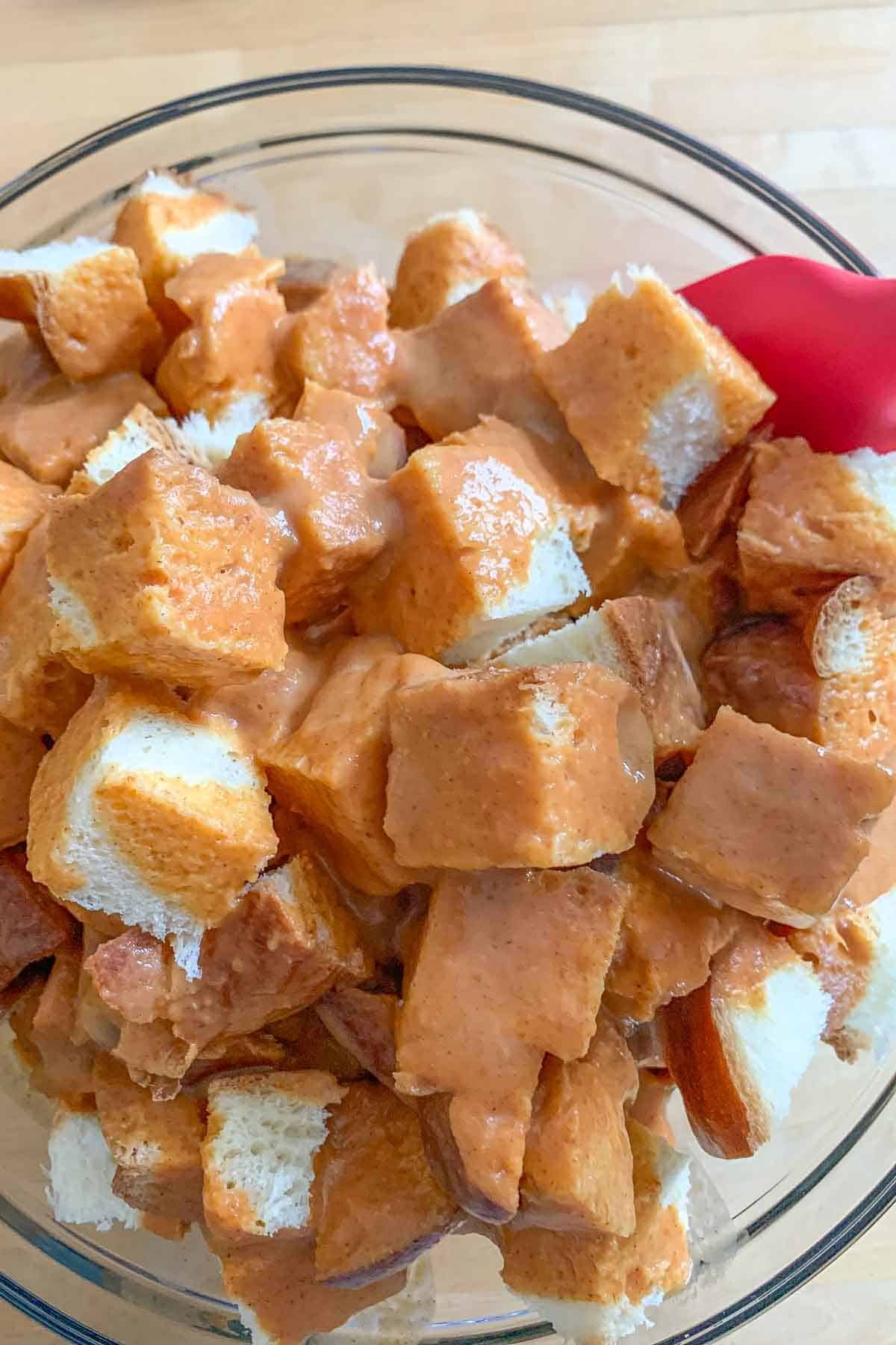 mixing bread cubes and french toast custard in a bowl