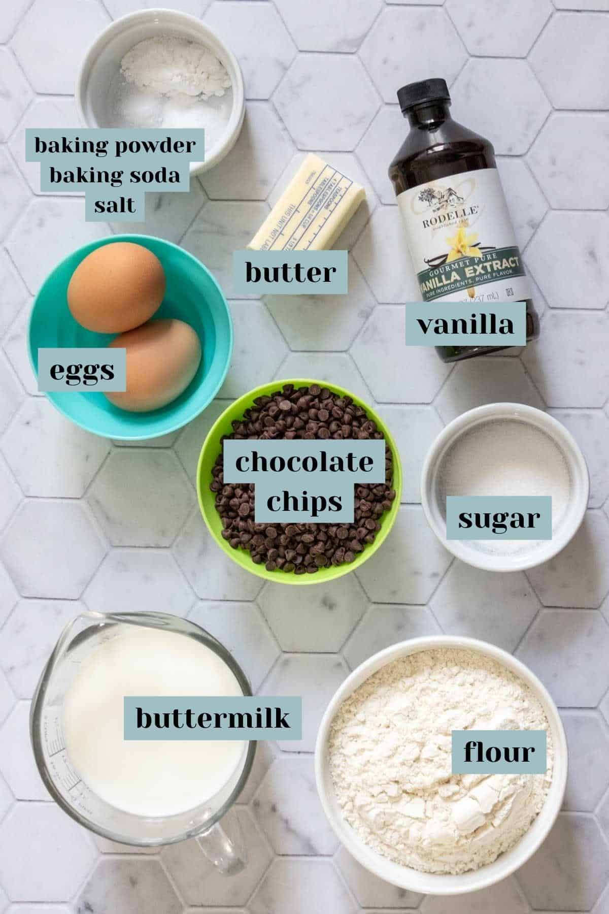 Ingredients for chocolate chip waffles and pancakes on a tile surface with labels.