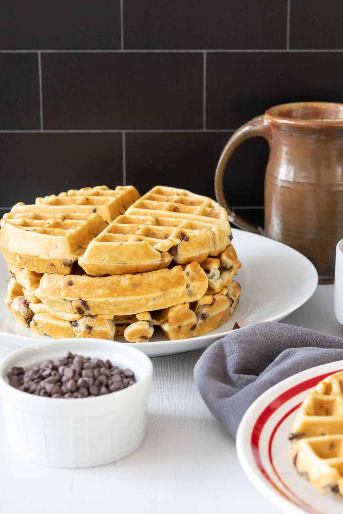 Plate with a stack of chocolate chip waffles and a white bowl of chocolate chips in front.