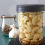 glass jar of pickled garlic with garlic and spices behind