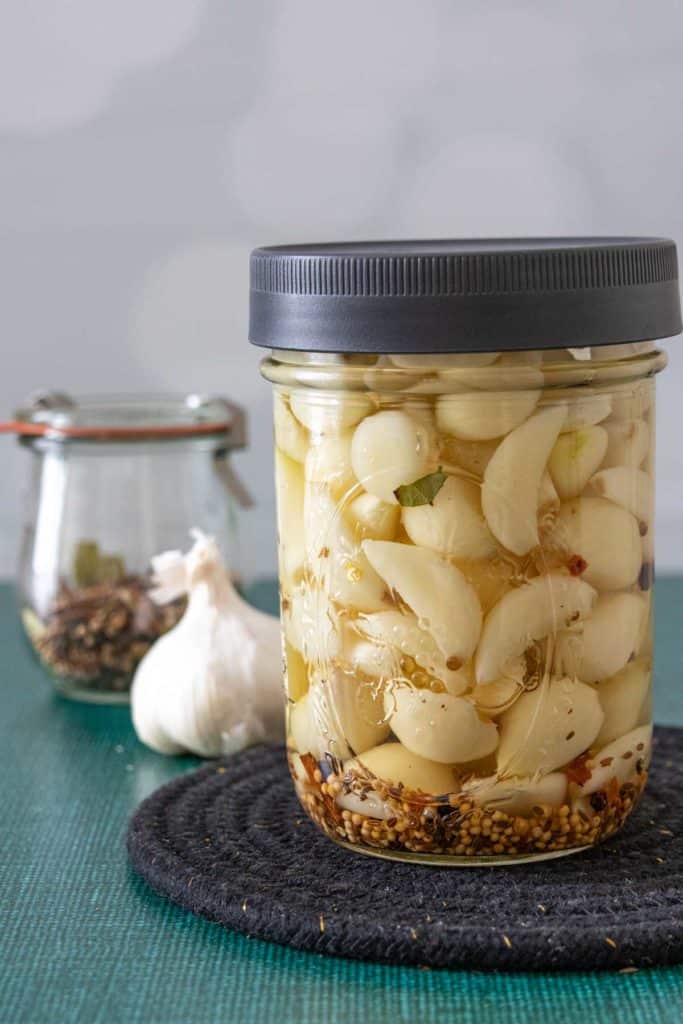 glass jar of pickled garlic with garlic and spices behind