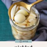 A spoon holds pickled garlic cloves above a jar of pickled garlic; garlic and spices sit in the background. Text reads "pickled garlic cloves.