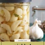 A jar of pickled garlic cloves sits on a counter next to a garlic bulb and a closed jar in the background, showcasing the vibrant appeal of homemade pickled garlic.