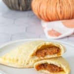 Pumpkin empanadas on a plate with one broken in half to see filling.