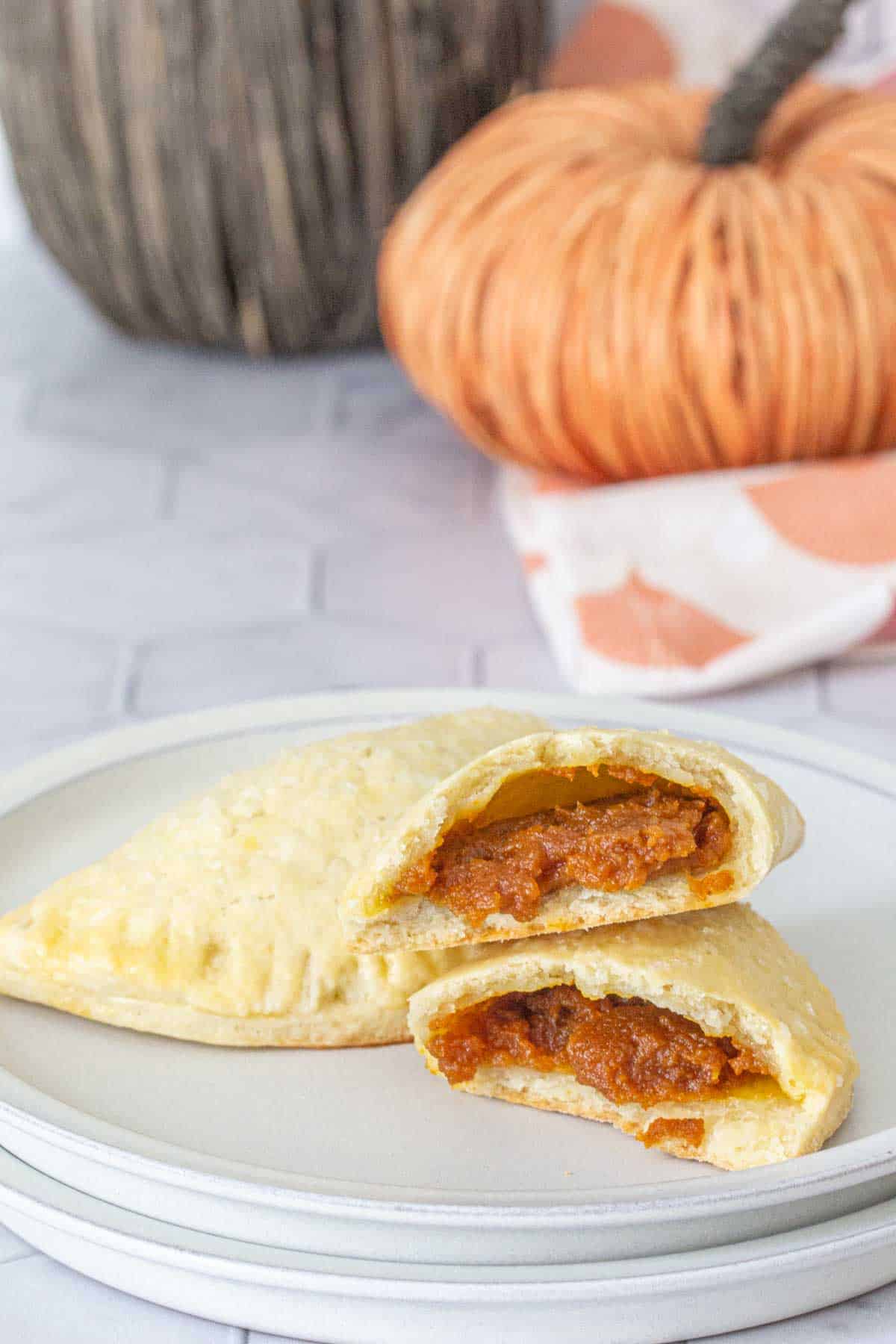 Pumpkin empanadas on a plate with one broken in half to see filling.