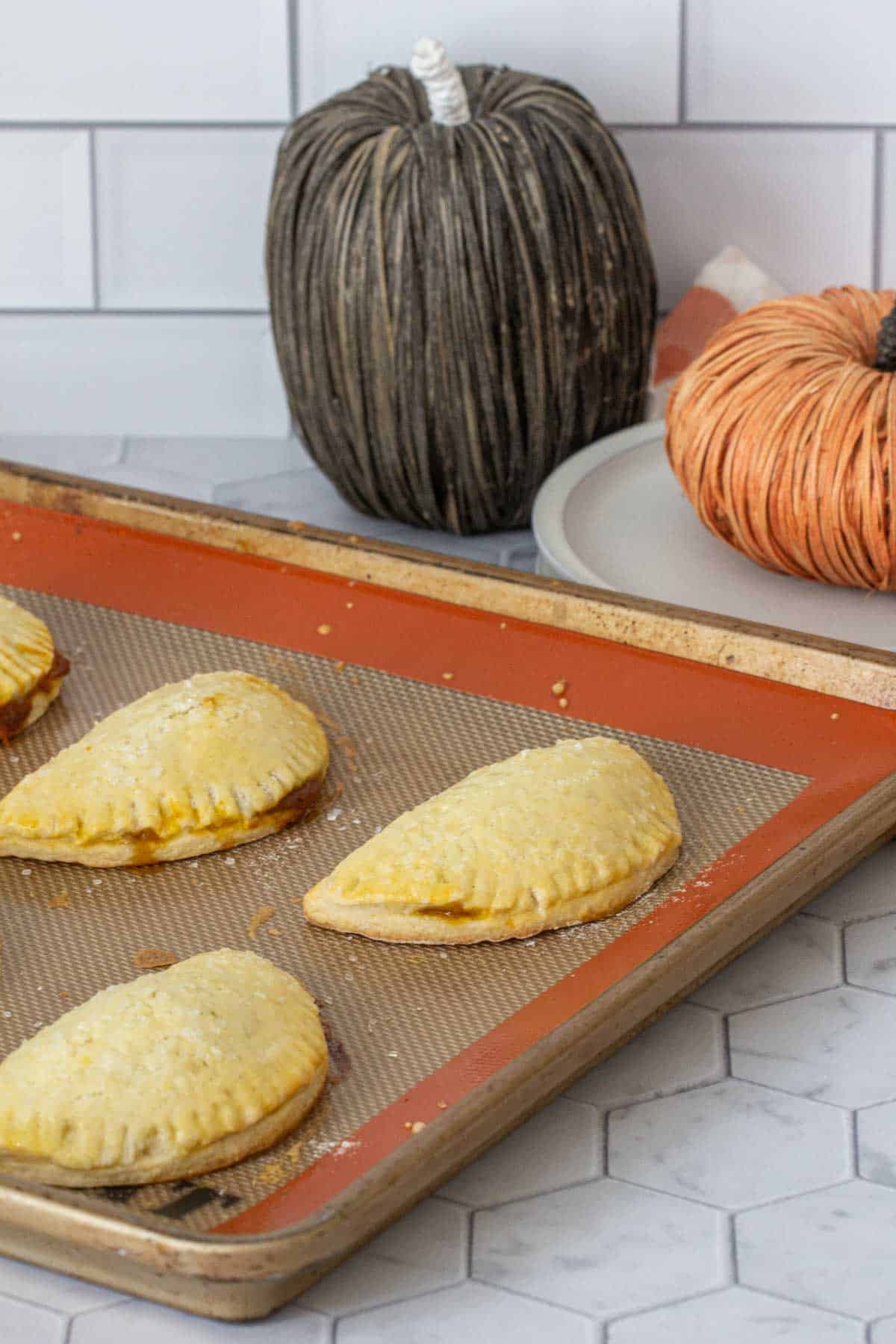 Baked pumpkin empanadas on a baking sheet.