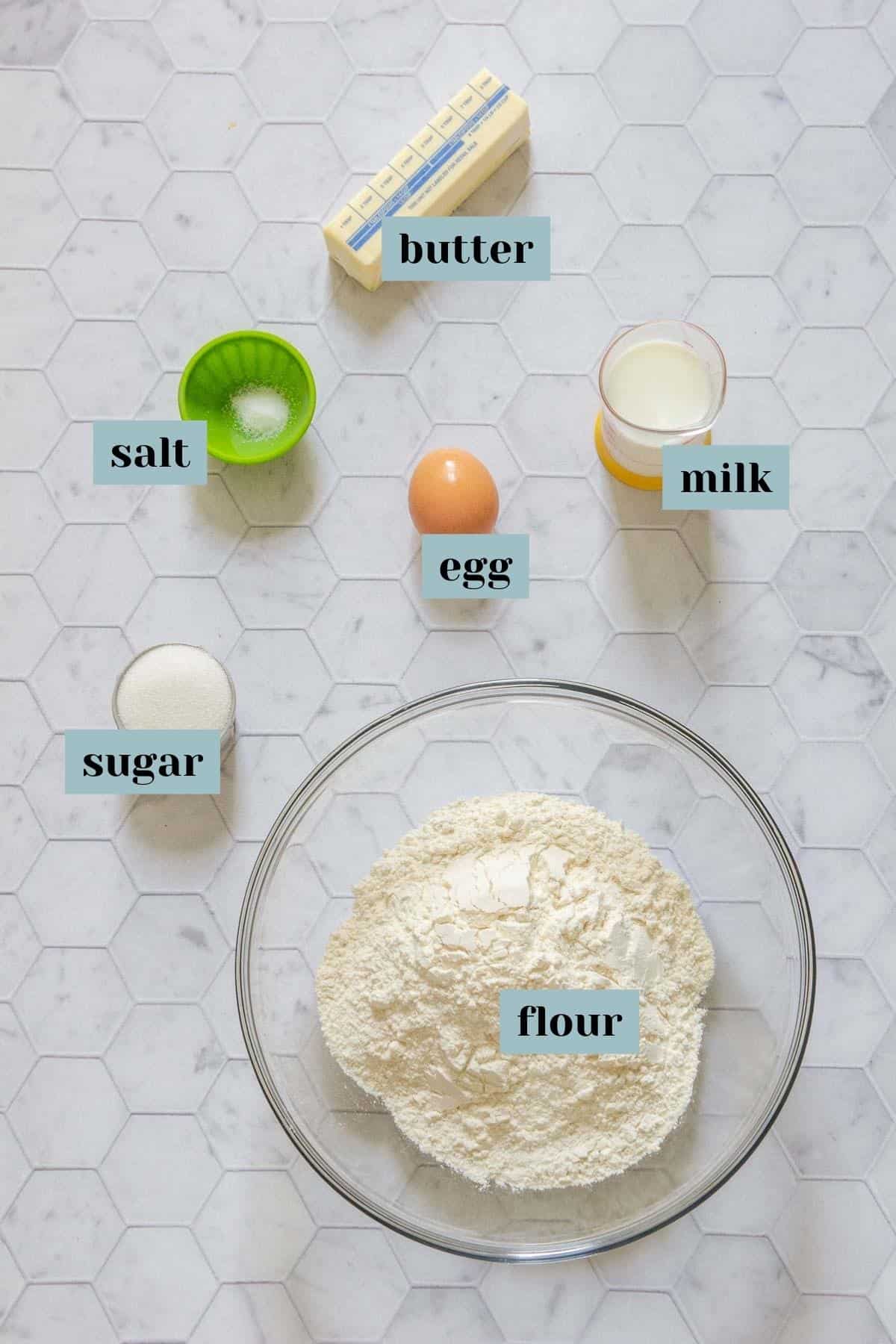 Ingredients for pumpkin empanada dough on a tile surface with labels.