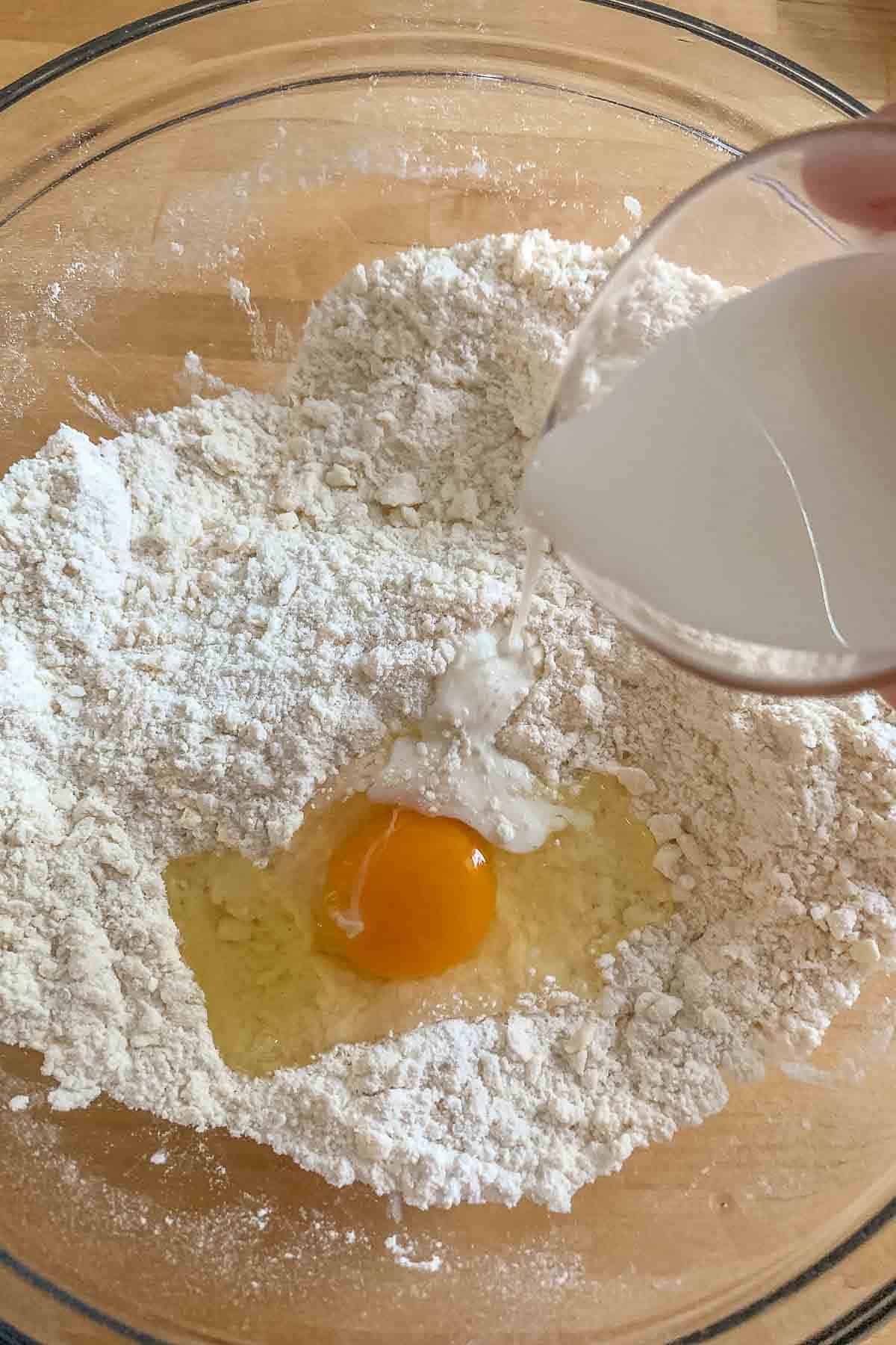 Adding milk and egg to empanada dough ingredients in a glass bowl.