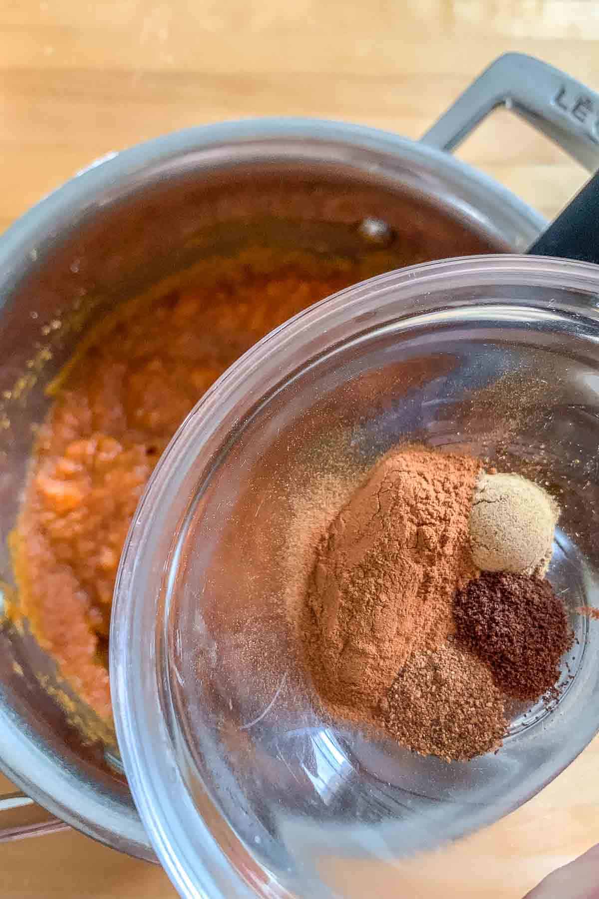 Spices in a small bowl being added to pumpkin empanada filling.